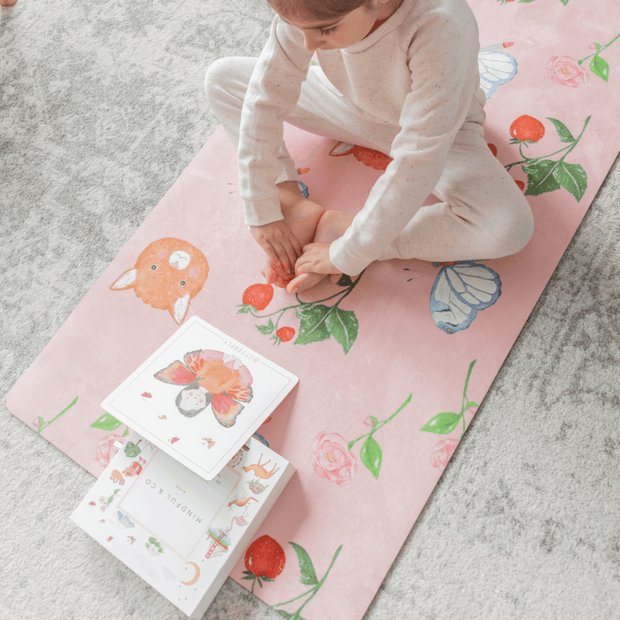 Child practicing on the Sweet Print Kids Yoga Mat with colorful illustrations and books nearby.