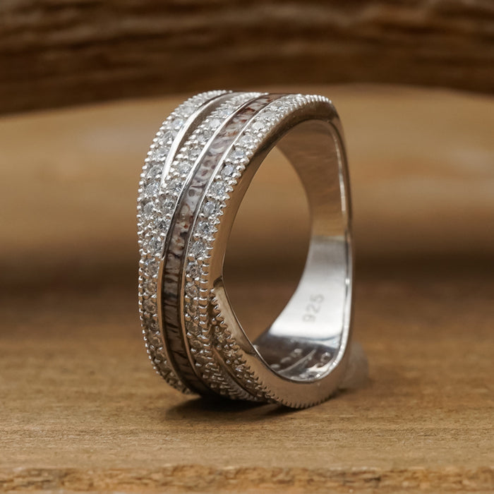 The Chelly is a sterling silver women’s band featuring multiple rows of small clear stones with a central row of champagne-colored stones, beautifully showcased against a blurred wooden background.