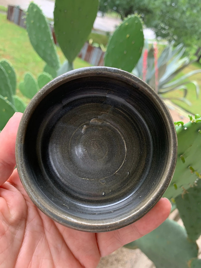 Three stacked THE IMMACULATE BEARD - SHAVE BOWL IN CHARCOAL by THE IMMACULATE BEARD, featuring handmade round ceramic bowls in dark gray with a matte finish and subtle horizontal ridges on a white reflective surface.