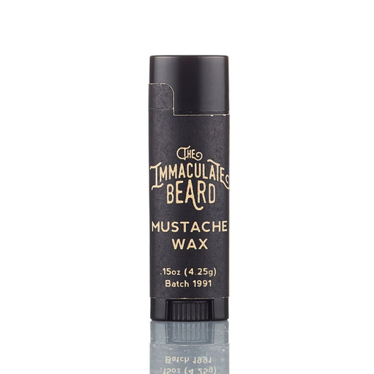 A black tube of THE IMMACULATE BEARD - UNSCENTED MUSTACHE WAX, 0.15 oz (4.25g), stands upright on a reflective surface against a white background. Ideal for natural beard grooming and styling handlebar mustaches. Batch 1991.
