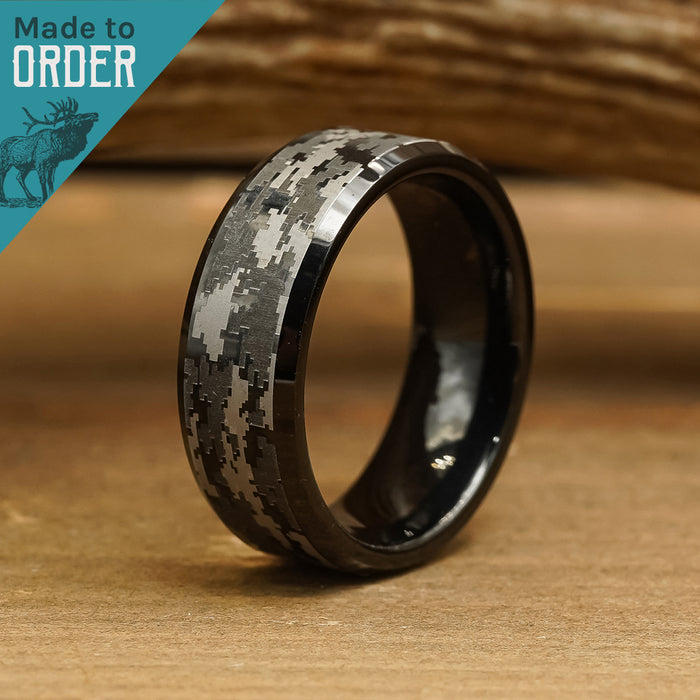 The Sarge, a black tungsten carbide ring featuring a bold digital camouflage pattern, stands upright on a wooden surface to showcase contemporary men's fashion. In the top left corner, a teal banner reading "Made to ORDER" appears alongside an illustrated elk.