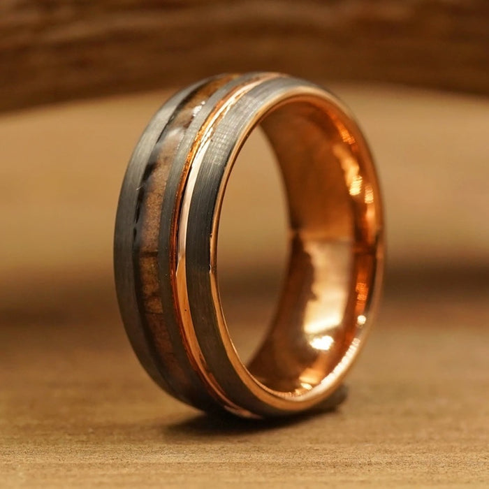 A close-up of The Tikal, an 8mm men's tungsten ring showcasing a brushed gunmetal grey band with a copper-colored inlay, resting upright on a wooden surface.