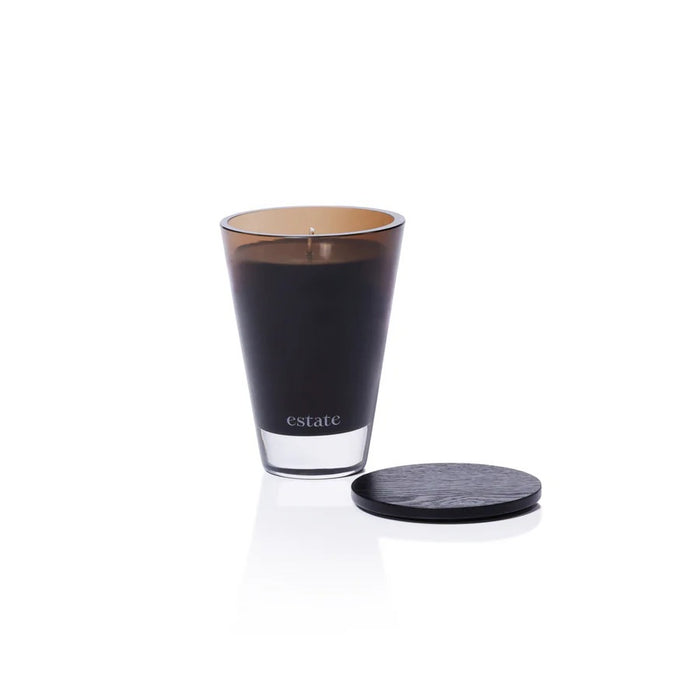 The ZODAX Thistle Estate Candle (10.5 oz) in black is displayed in a glass holder beside its matching box, both reflecting the fresh California coast fragrance.