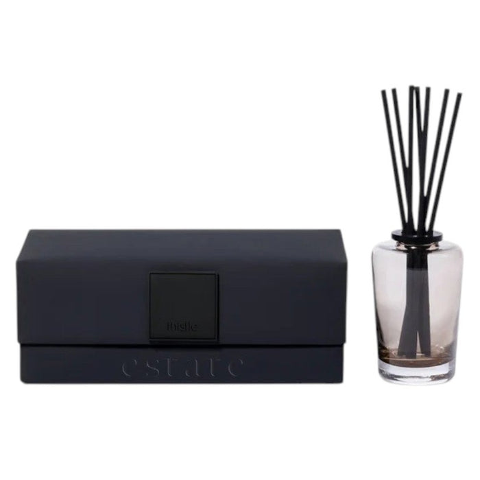 A black rectangular ZODAX gift box with a small label sits beside the THISTLE ESTATE DIFFUSER - 200 ML, featuring black reeds and scented liquid for a refreshing California coast fragrance.