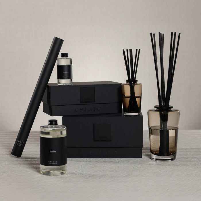 A black rectangular ZODAX gift box with a small label sits beside the THISTLE ESTATE DIFFUSER - 200 ML, featuring black reeds and scented liquid for a refreshing California coast fragrance.