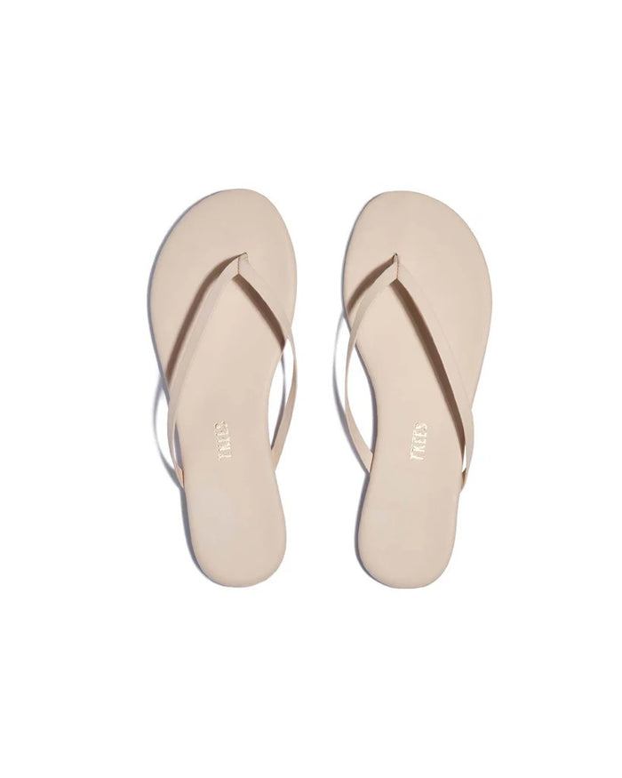 The TKEES INC FOUNDATIONS SLIPPER MATTE LINEN features beige minimalist flip-flops with thin straps, handcrafted from buttery-soft leather, shown side by side on a white background.