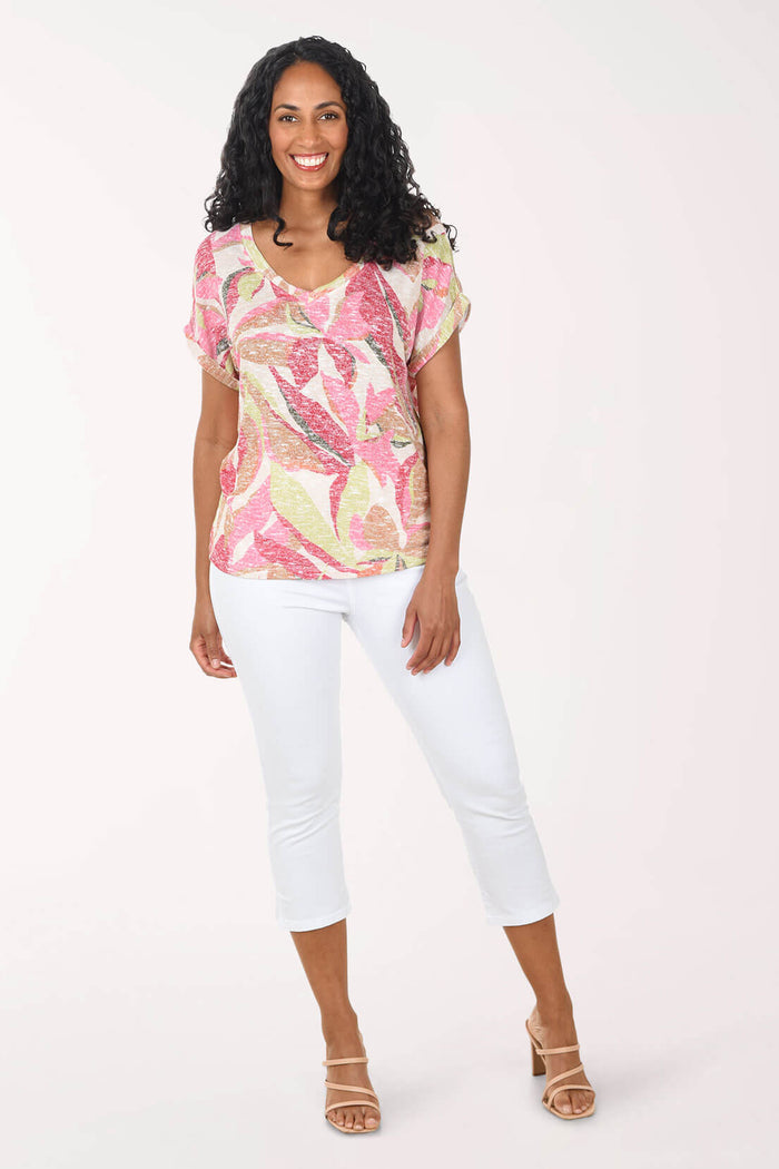 Woman wearing a printed top and white capri pants against a light pink background