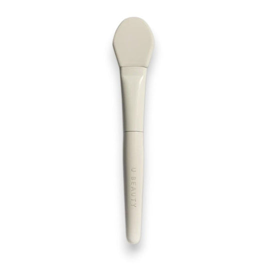 THE BRUSH by U BEAUTY is a white silicone skincare applicator featuring a flat, rounded tip and "U BEAUTY" on the handle—crafted for precision application against a clean, white background.