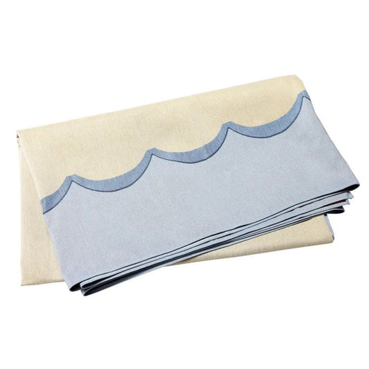 The VIETRI Tavola Scalloped Tablecloth in blue features a beige jacquard fabric with light blue scalloped edges, neatly folded on a flat surface.