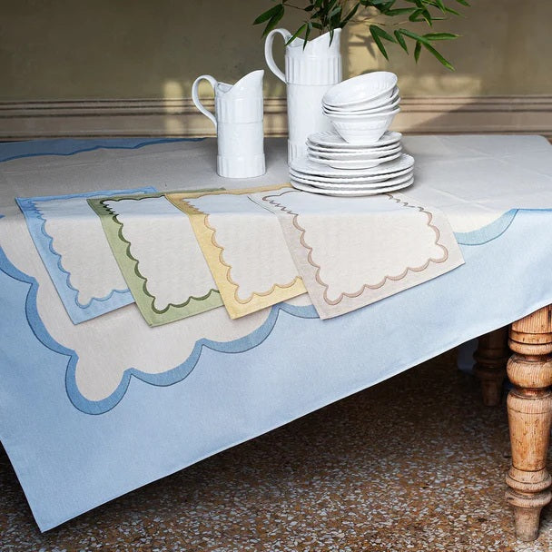 The VIETRI Tavola Scalloped Tablecloth in blue features a beige jacquard fabric with light blue scalloped edges, neatly folded on a flat surface.
