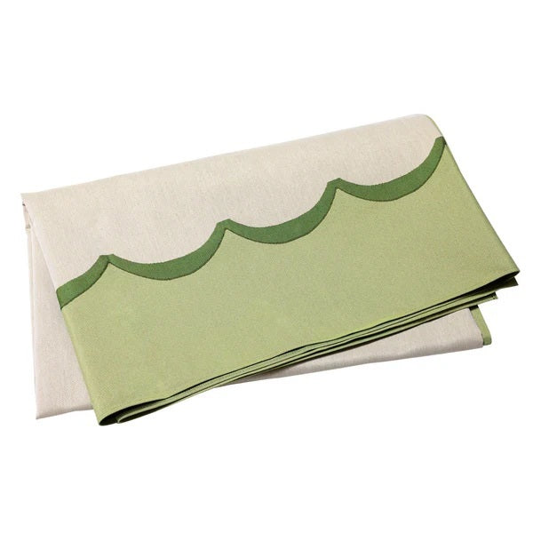 Four linen napkins in blue, green, yellow, and beige with embroidered scalloped edges are layered on a white surface beside the VIETRI - TAVOLA SCALLOPED TABLECLOTH in green, adding vibrant color and highlighting their detailed borders.