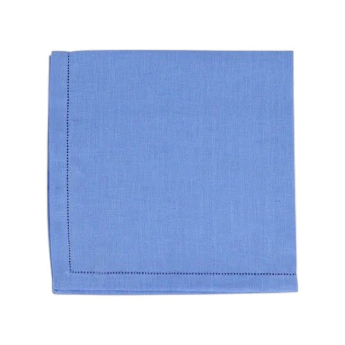 The VIETRI Tessuti Dinner Napkin in Cornflower Blue rests on a vibrant tablecloth with red, beige, and green geometric patterns outlined in white, bringing elegance to your VIETRI table linen collection.