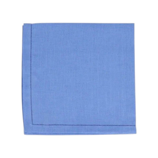 The VIETRI Tessuti Dinner Napkin in Cornflower Blue rests on a vibrant tablecloth with red, beige, and green geometric patterns outlined in white, bringing elegance to your VIETRI table linen collection.