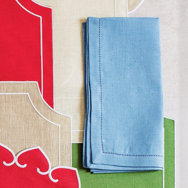 The VIETRI Tessuti Dinner Napkin in Cornflower Blue rests on a vibrant tablecloth with red, beige, and green geometric patterns outlined in white, bringing elegance to your VIETRI table linen collection.