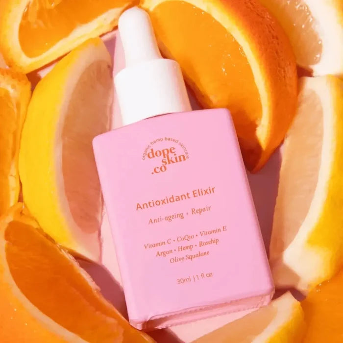 Pink bottle of 'dope skin co' Antioxidant Elixir surrounded by sliced oranges