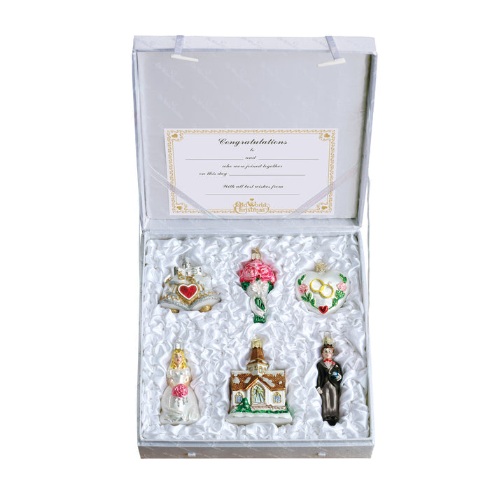 A silver gift box with a â€œCongratulationsâ€_x009d_ card inside the lid, displaying six wedding-themed figurines: a decorated cake, a bouquet, wedding rings, a bride, a church, and a groom, all nestled in white satin lining.