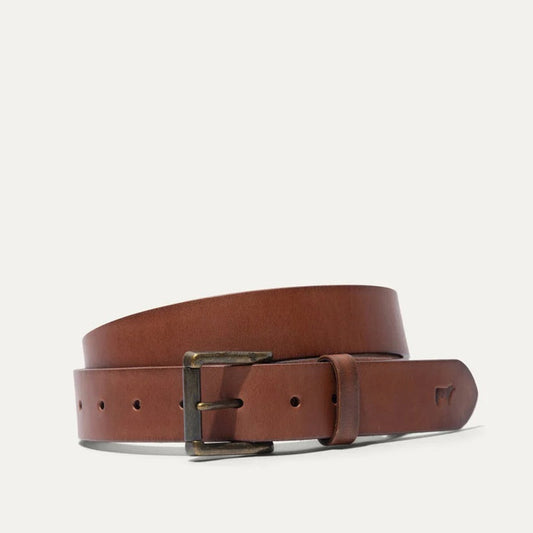 A close-up of the WILL LEATHER GOODS – SADDLE BELT IN COGNAC shows its full grain leather, five holes, and a small embossed animal logo near the tip, displayed on a plain white background.