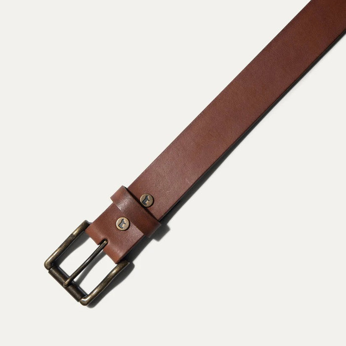 A close-up of the WILL LEATHER GOODS – SADDLE BELT IN COGNAC shows its full grain leather, five holes, and a small embossed animal logo near the tip, displayed on a plain white background.