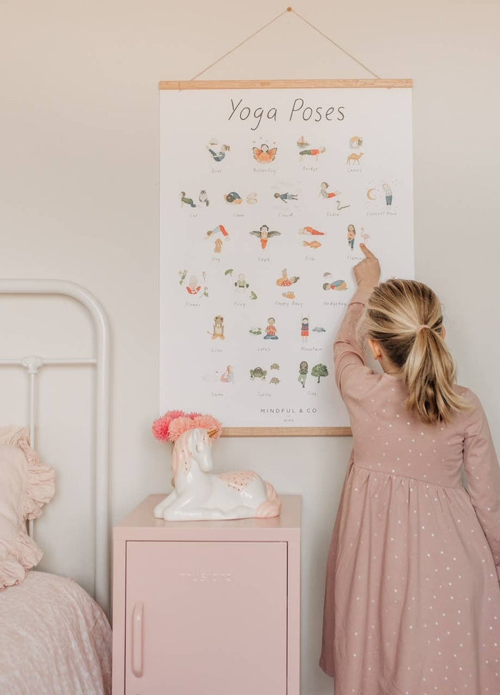 Child pointing at Yoga Poses Print educational poster featuring fun yoga poses for kids.