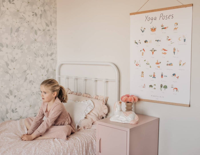 A child practicing yoga beside a colorful Yoga Poses Print poster in a cozy bedroom setting.